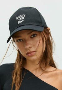 Schwarze Kappe mit dem Aufdruck "MESSY HAIR DAY" in Weiß, ausgestattet mit einer strukturierten Krone und gebogenem Schild, aus einem glatten Stoff gefertigt.