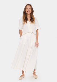 Ensemble à deux pièces blanc comprenant un haut à manches courtes avec un devant boutonné et une longue jupe fluide avec une bordure en dentelle. Conçu en tissu léger.
