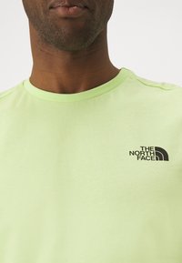Světle zelené bavlněné tričko s kulatým výstřihem a malým černým logem "The North Face" v horním levém rohu.