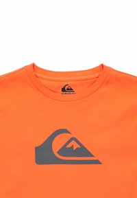 Oranžové bavlnené tričko s tmavosivým logom na prednej strane, zahŕňajúce tvar vlny a hory, s okrúhlym výstrihom.