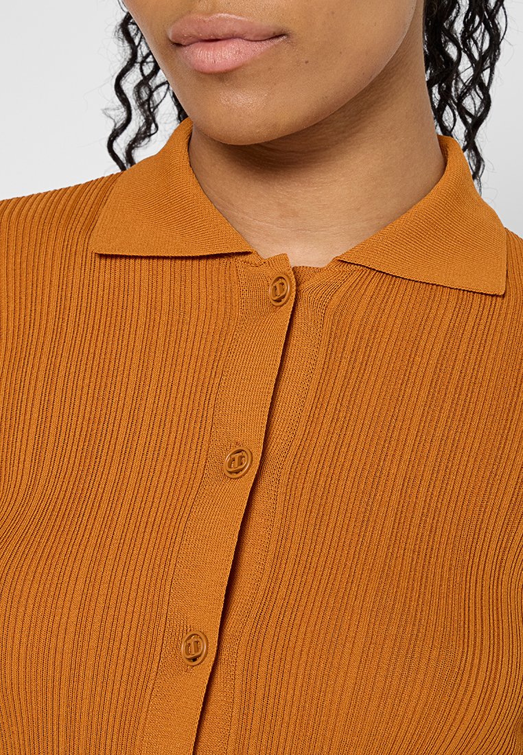 Rippstrick, oranges Strickshirt mit Polo-Kragen, versehen mit zwei runden Knöpfen vorne, glatte Textur und eng anliegendem Schnitt.