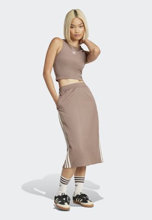 Lys brun crop top og matchende lang skjørt med hvite sidestriper. Modell som bruker svarte og kremfargede sko med stripete sokker.