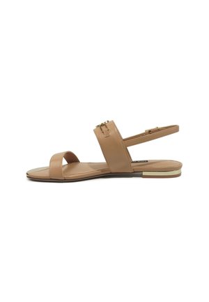 Beige flat sandal with open toe, ankle strap, gold buckle, and a small gold accent on the heel, displayed on a white background.