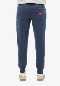 Marineblå sweats, lavet af blød stof, med en baglomme med et rødt mærke, tapered cuffs og en behagelig pasform. Sneakers er ikke inkluderet.