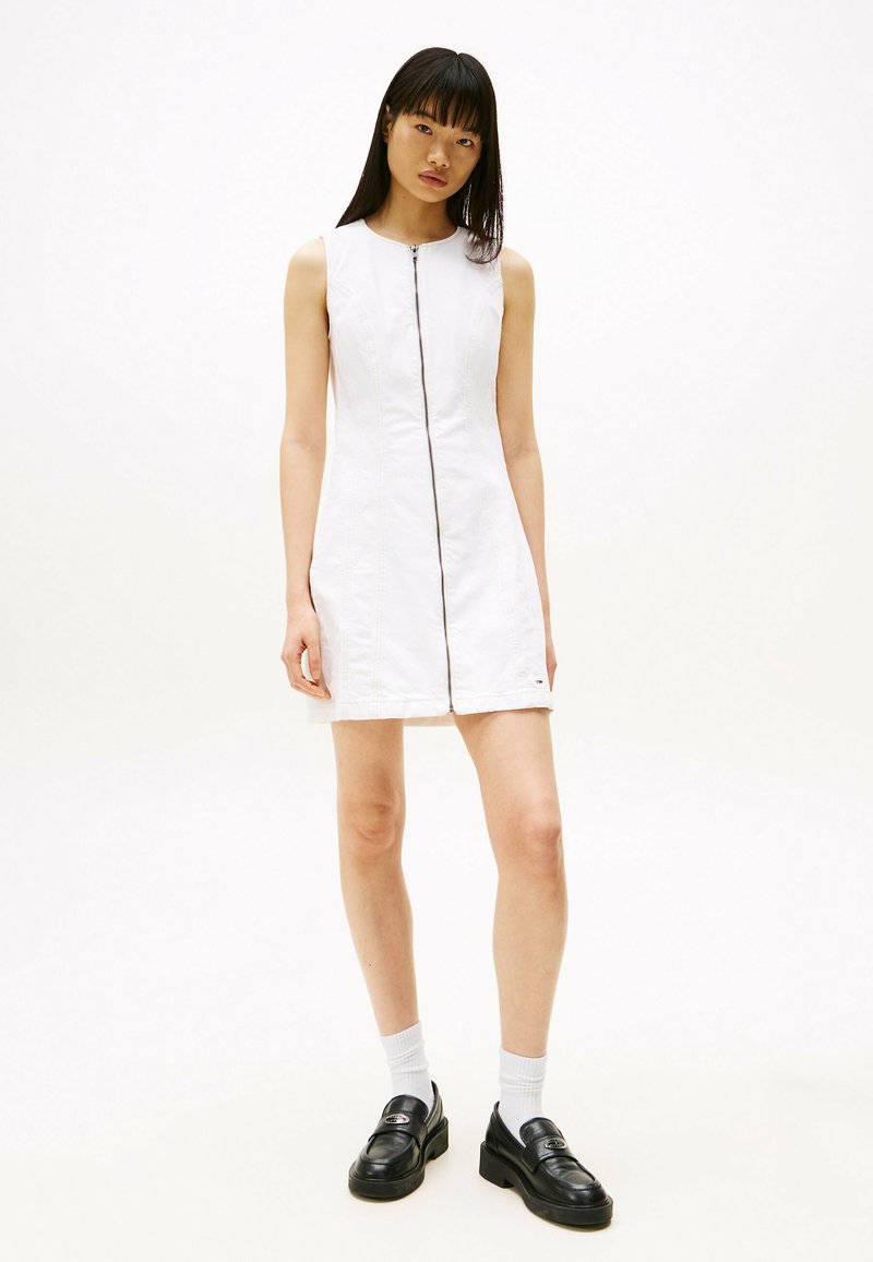 Biała sukienka bez rękawów z zamkiem z przodu, z bocznymi szwami. Stylizowana z czarnymi loafersami na platformie i białymi skarpetkami.