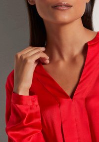 Rode satijnen blouse met een V-hals, lange mouwen en knoopmanchetten. De gladde textuur en subtiele glans benadrukken het elegante ontwerp.