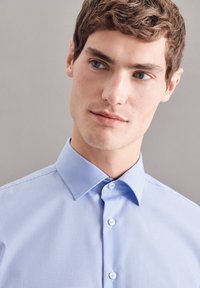 Lichtblauw geruit shirt met een klassieke kraag en knoopsluiting. Glad textuur, met kleine ruitjes en contrasterende witte knopen.