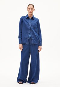 Denim outfit met een button-up shirt met een borstzak en wide-leg broek. De stof is effen donkerblauw met een gladde textuur.