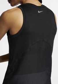 Svart atletisk linne i mjukt tyg med en meshinläggning på baksidan. Har en liten reflekterande logotyp på den övre bakre halslinningen.