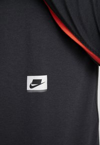Gros plan d’un tissu noir avec un petit patch carré blanc présentant un logo Nike noir et une bordure rouge visible sur le bord.
