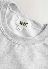 Hallitus hall sweatshirt krae ribitud tekstuuriga. Sildil on mustades tähtedes kiri "self.". Kangas näib pehme ja õrna helesinise mustriga.
