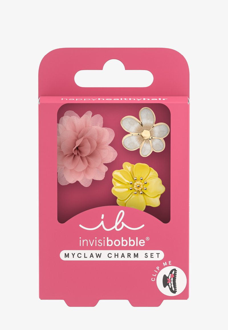 Three flower-shaped hair charms—a pink fabric flower, a white and gold metal flower, and a yellow glossy flower—in pink packaging.