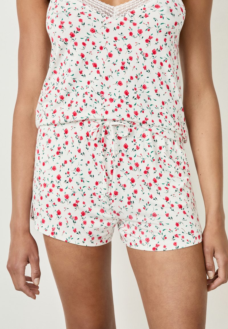 Ensemble de pyjama blanc à fleurs comprenant un top sans manches et un short, orné de roses rouges et de feuilles vertes, avec une taille à cordon et des accents en dentelle.