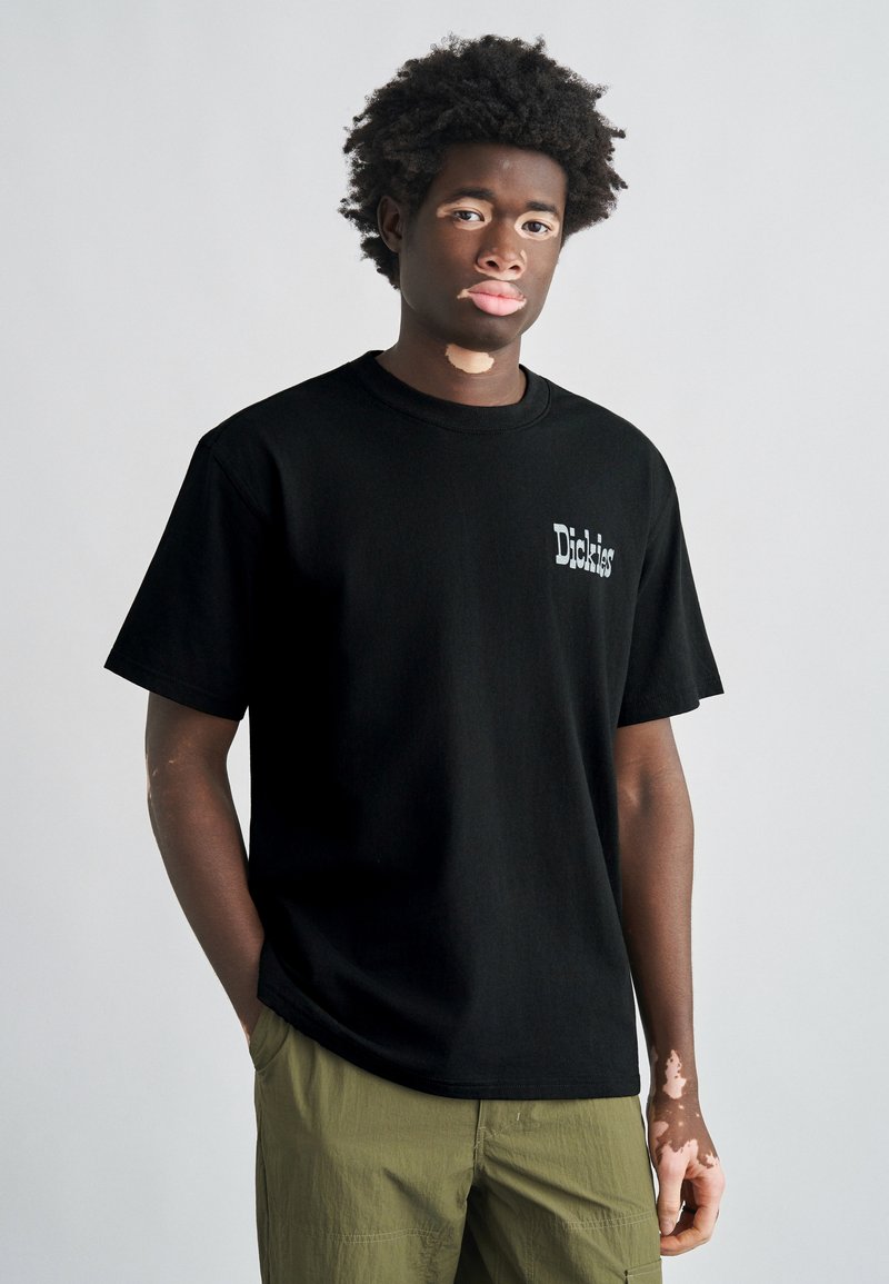 Black short-sleeve T-shirt made of cotton, featuring a small white "Dickies" logo on the left chest area; paired with olive green cargo shorts.