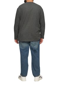 Grijze lange mouwen shirt met een gespikkelde textuur, gecombineerd met lichtblauwe jeans en witte sneakers met blauwe accenten. Gezien vanuit de achterkant.