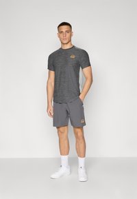 Gray heathered athletic T-shirt with a small logo, paired with solid gray shorts. Model wearing white athletic shoes and socks.