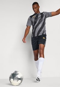 Grå og svart stripete sportsjersey med korte ermer, sammen med svarte shorts. Hvite knestrømper og en svart-hvit fotball på bakken.