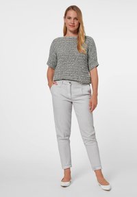 Grijze gebreide top met korte mouwen, gecombineerd met lichtgrijze, strakke broeken. De broeken hebben plooien aan de voorkant en opgerolde broekspijpen. Draagt het met witte platte schoenen.