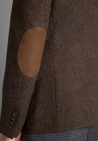 Blazer in tweed marrone con tessuto strutturato. Presenta toppe in camoscio brown a contrasto sui gomiti e dettagli con quattro bottoni ai polsini. Vestibilità tailored.