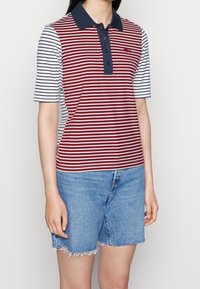 Polo rayé rouge et blanc avec col bleu marine, manches courtes et petit logo. Associé à un short en jean bleu clair.