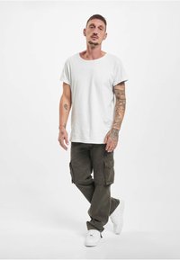 Hvit bomulls-T-skjorte med avslappet passform, kombinert med olivengrønne cargobukser med sidelommer. Fottøy: hvite joggesko.