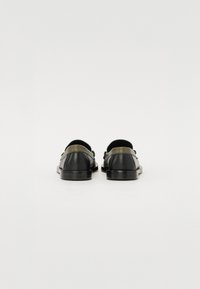 Chaussures noires en cuir à texture lisse, avec des accents verts et un design épuré, des coutures visibles et une semelle profil bas.