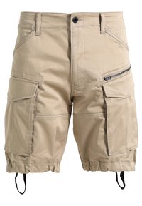 Shorts cargo beiges avec plusieurs poches, y compris des poches à fermeture éclair et à rabat, ourlets élastiques avec cordon de serrage, et passants pour ceinture à la taille.