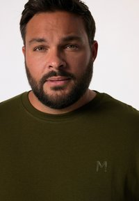 Olivově zelené bavlněné tričko s kulatým výstřihem a malým embosovaným logem na levé straně hrudi. Hladká textura, krátké rukávy.