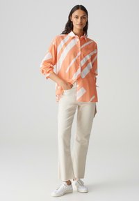 Camicia a righe color corallo e bianco, maniche lunghe, vestibilità rilassata. Abbinata a pantaloni color crema e sneaker bianche.
