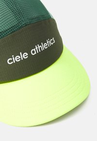 Grön och neongul sportmössa med texturerad tyg och "ciele athletics" tryckt i vitt på frampanelen.