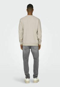 Lys beige sweatshirt med rund hals, ribbede manchetter og kant i bunden, sammen med grå jeans og hvide sneakers, set bagfra.