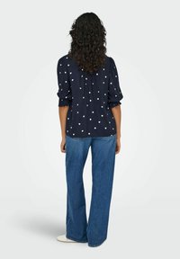 Marineblå bluse med hvidt hjerte-mønster, har puffede ærmer og en samlede ryg; parret med lyseblå flagrende jeans.