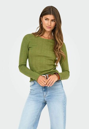 Langærmet grøn bluse med ribbet tekstur, rund halsudskæring og takkede manchetter, parret med lys blå denimjeans.