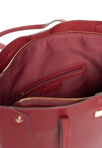 Rote Lederhandtasche mit strukturierter Außenfläche, glattem Innenfutter, einem Reißverschlussfach und eleganten goldfarbenen Metallakzenten.