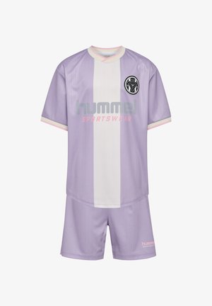 To smilende børn står side om side og holder hænder, iført matchende lilla og hvide sportstøj med blå sneakers.