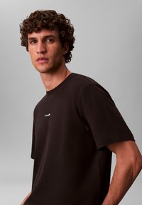 Mustast puuvillast T-särk ümmarguse kaelusega ja lühikeste varrukatega, rinnal väike valge logo, sile pind ja lõdvestunud istuvus.