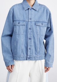 Light blue denim jacket featuring a collared neck, two front pockets, and button closures, with a relaxed fit and subtle stitching details.