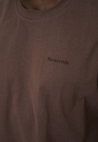 Brun kortærmet t-shirt lavet af blødt stof, med rund halsudskæring og et lille, mørkt trykt logo på brystet.
