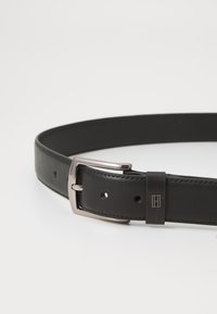 Curea din piele neagră cu o textură elegantă și netedă, având o cataramă dreptunghiulară din metal argintiu și mai multe găuri pentru ajustare.
