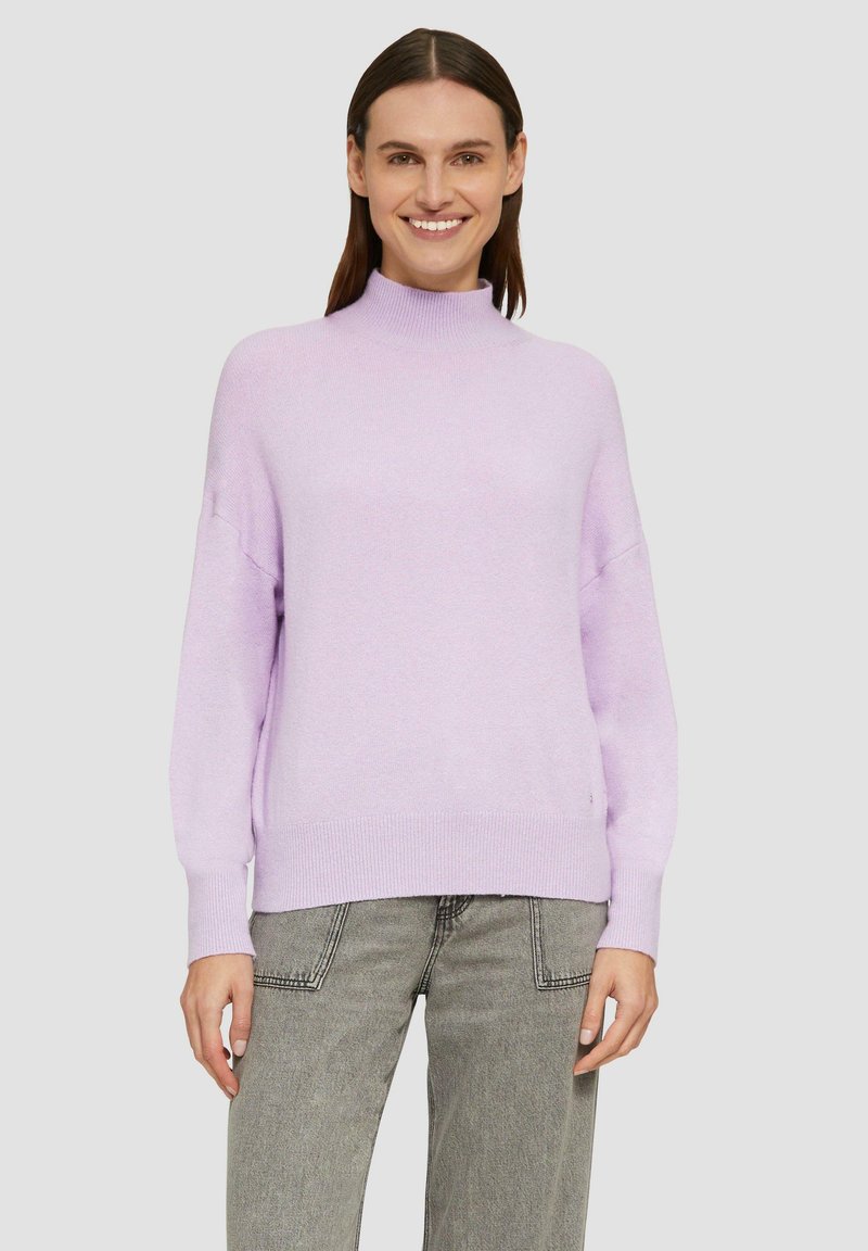 Helllila Pullover mit hochgeschlossenem Kragen und langen, lockeren Ärmeln; weicher Stoff und gerippter Saum. Kombiniert mit grauen Jeans.