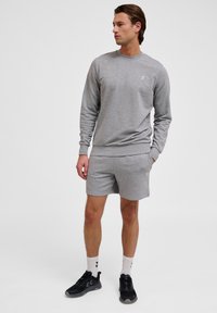 Sweatshirt gris avec un col rond et des poignets côtel�és, associé à un short gris assorti. Porté avec des chaussures de sport noires et des chaussettes blanches.