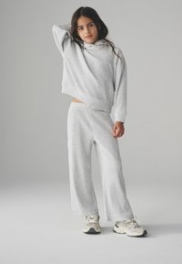 Lys grå ribbet hyggetøjssæt bestående af en kort hoodie og vide bukser. Materialet har en blød tekstur og vises med sneakers.