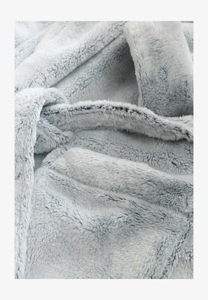 Vaaleanharmaa keinoturkista valmistettu lämmittelyhuopa, jossa on pehmeä, teksturoitu pinta, joka tuo esiin ylellisen tuntuman ja hellävaraisen kiillon, laskostettuna, paljastaen vaihtelevaa syvyyttä.