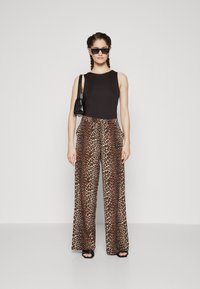 Top preto sem mangas combinado com calças largas de estampa de leopardo em bege e castanho, apresentando uma textura suave e bolsos laterais. Óculos de sol pretos e bolsa.