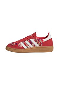 Zapatilla Adidas roja con rayas blancas, patrón floral en los paneles de tela, suela de goma y detalles de gamuza en la punta y el talón.