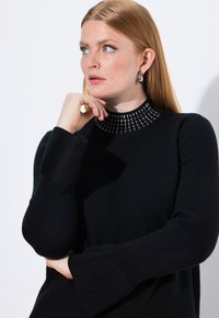 Czarny sweter z wysokim dekoltem ozdobionym metalowymi akcentami. Posiada długie rękawy z szerokimi mankietami oraz miękką fakturę.