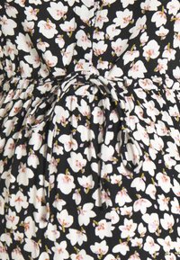 Tissu noir avec de petits motifs floraux blancs et roses, avec des plis à la taille et un détail de ceinture nouée. Texture douce, design floral.