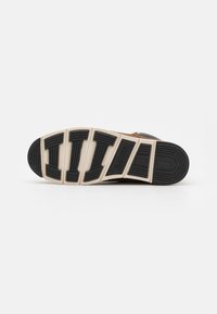 Zwarte rubberen zool met een getextureerd loopvlakpatroon, crèmekleurige tussenzool en bruine accenten. Casuale sneaker onderaanzicht, met een stevige uitstraling.