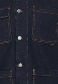 Dark blue denim shirt with two chest pockets, silver snap buttons, and contrasting orange stitching. Smooth texture, classic design.