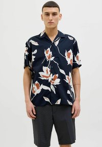 Camisa de manga corta en azul marino con un gran patrón floral blanco y naranja; presenta un cierre de botones en la parte delantera y un cuello, hecha de tejido ligero.
